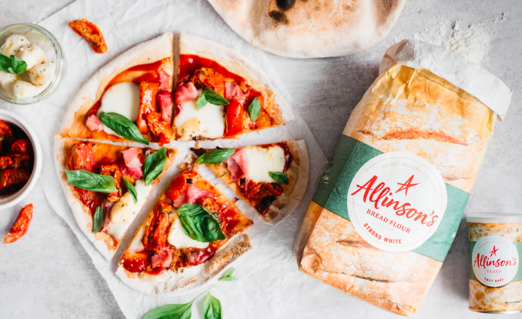 A home made pizza sits on a table, alongside a pack of Allinson's Strong White Bread Flour and Allinson's Yeast.