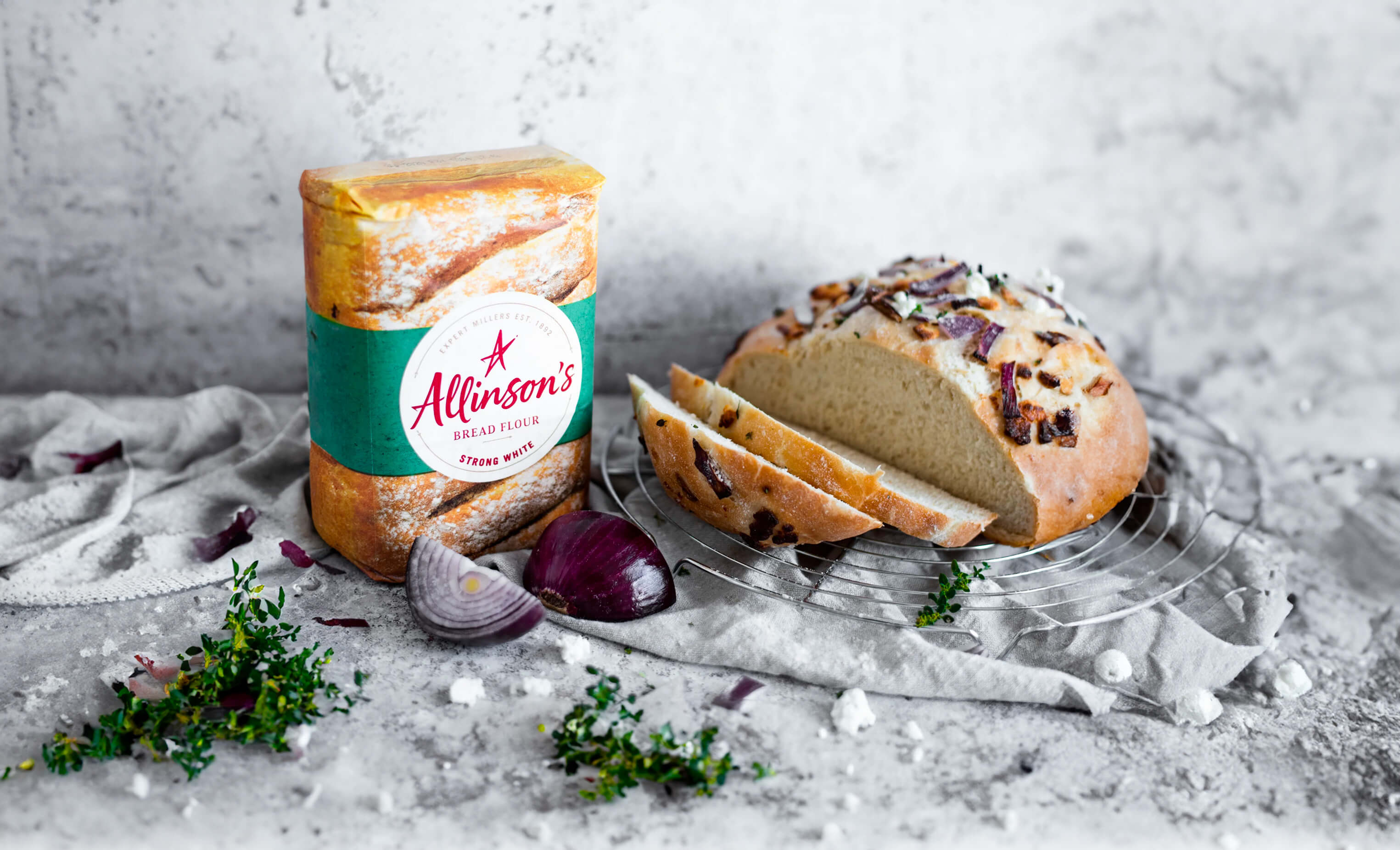 A pack of Allinson's Strong White Bread Flour next to a sliced freshly baked red onion and goats cheese loaf.