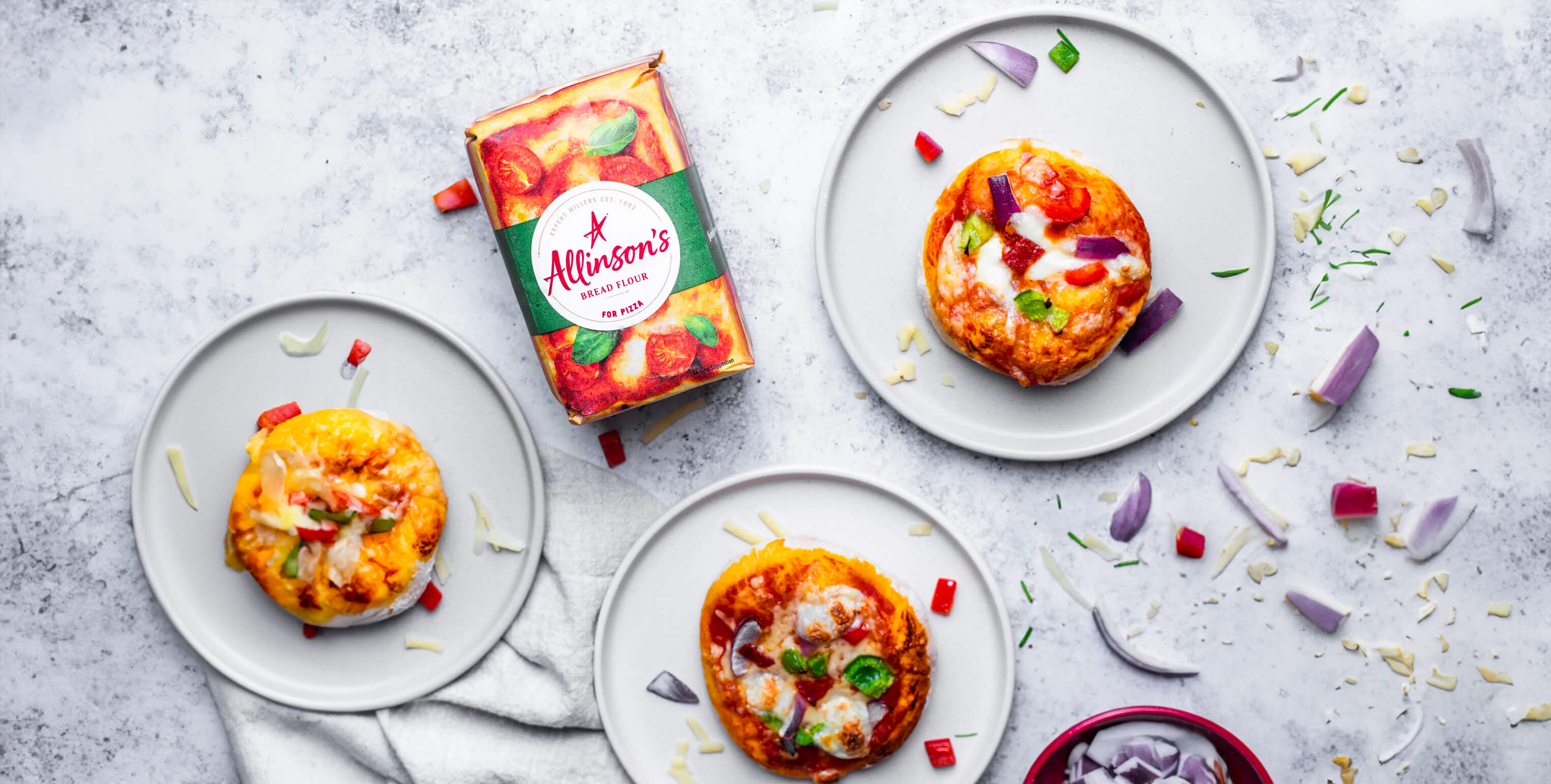 A pack of Allinson's Bread Flour for Pizza, surrounded by mini pizzas topped with mozzarella and colourful slices of pepper and red onion.