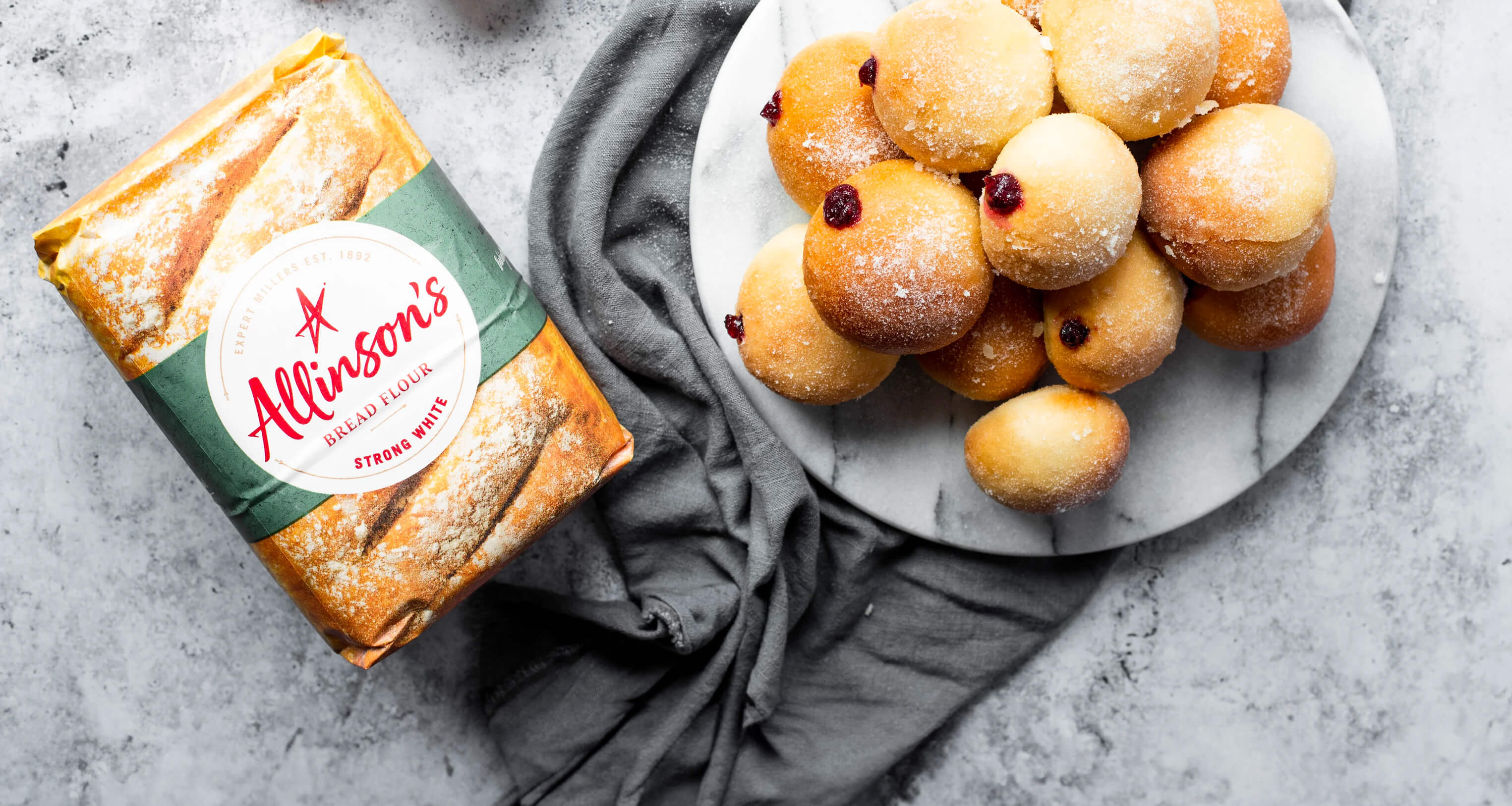A plate piled with baked doughnuts oozing jam, alongside a pack of Allinson's Strong White Bread Flour.